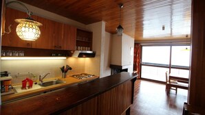 Une cuisine avec des meubles de rangement en bois, une cuisinière à gaz et un évier. On y trouve également un coin repas avec une table et des chaises.