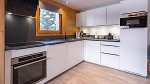 Una cocina moderna con armarios blancos, horno empotrado y ventana con vistas a árboles.