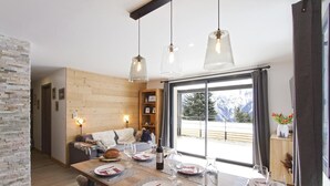 Ein Essbereich mit Holztisch, gedecktem Tisch für eine Mahlzeit, einer Couch mit Decken und Blick auf Berge durch große Fenster.