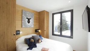Ein Schlafzimmer mit einem großen Bett, einem hölzernen Kopfteil, einer Wanddekoration von Hirschgeweihen, einem Fenster mit Blick auf Bäume und einem angebrachten Fernseher.