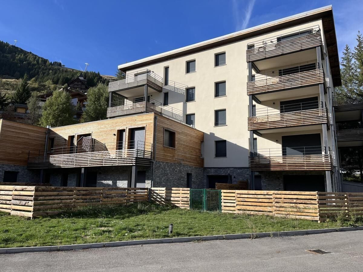 A modern multi-story building with balconies, a stone facade, and a wooden deck area.