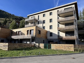 A modern multi-story building with balconies, a stone facade, and a wooden deck area.