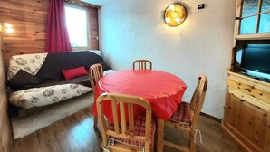 Una habitación acogedora con suelo de madera, una mesa redonda con cubierta roja y un sofá con cojines estampados.