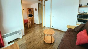 Una sala de estar con un sofá marrón, una mesita de madera y una cocina al fondo.