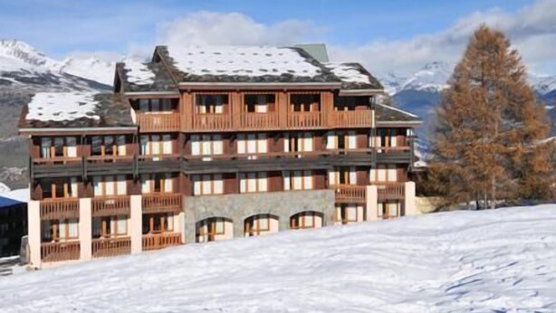 Un hotel a più piani con balconi, sullo sfondo di una montagna innevata.