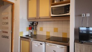 Una cucina compatta con microonde, lavastoviglie e un piccolo lavello. Ci sono pensili sopra il piano di lavoro e uno scaffale con utensili da cucina.
