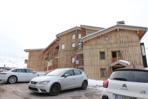 Un edificio de madera de varios pisos con balcones, coches aparcados y una montaña nevada al fondo.