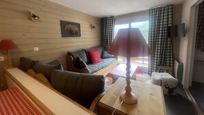 Ein gemütliches Wohnzimmer mit einer Couch, einem Holztisch mit Lampe und einem an der Wand befestigten Fernseher.