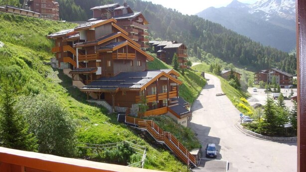 Ein mehrstöckiges Holzhaus mit Balkonen, gelegen an einem Hang mit Blick auf ein Gebirge.