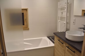 Une salle de bain moderne avec une baignoire, un meuble-lavabo en bois et une fenêtre avec des volets en bois.