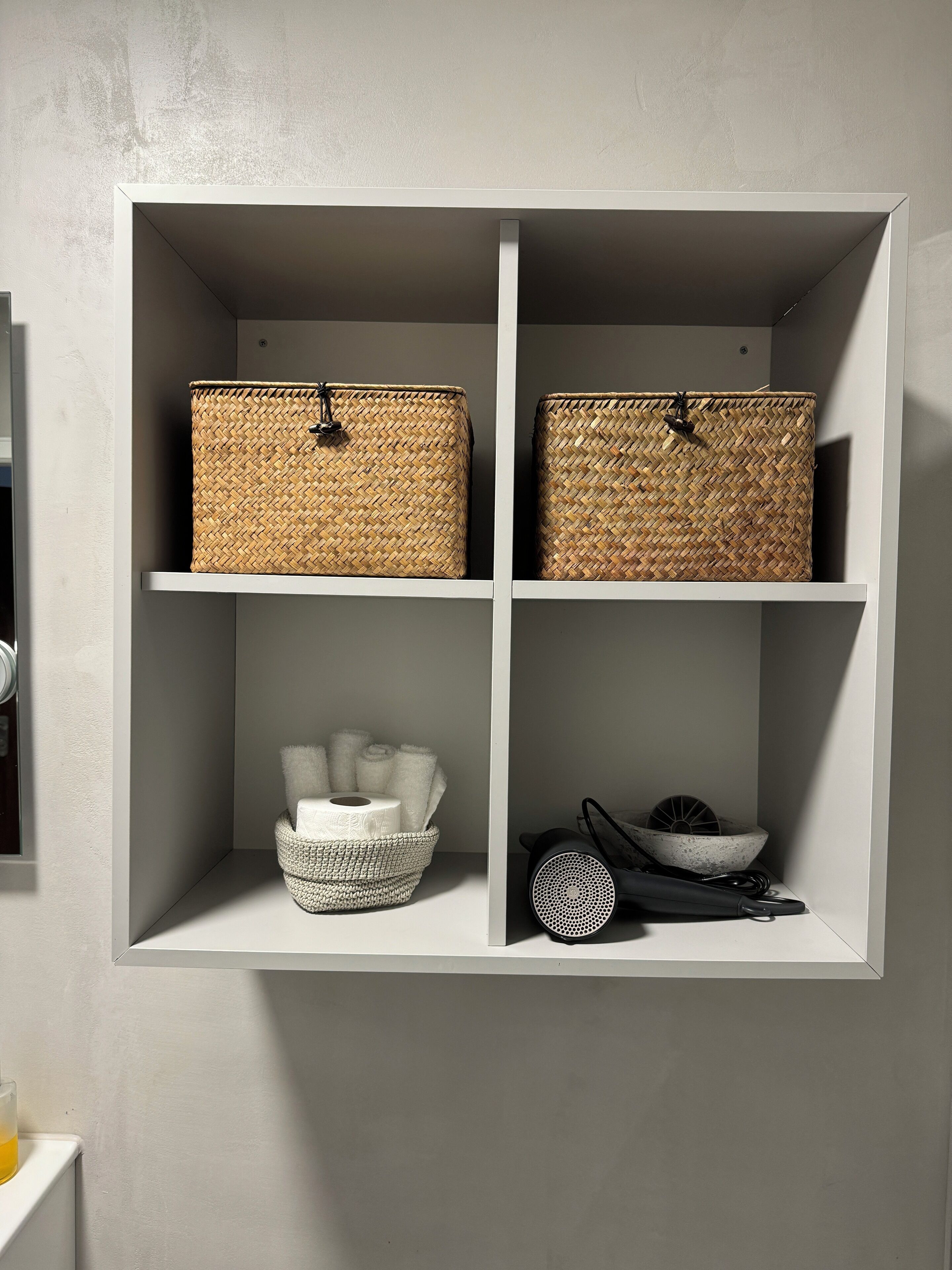 A white shelving unit with woven baskets and a bowl of towels.
