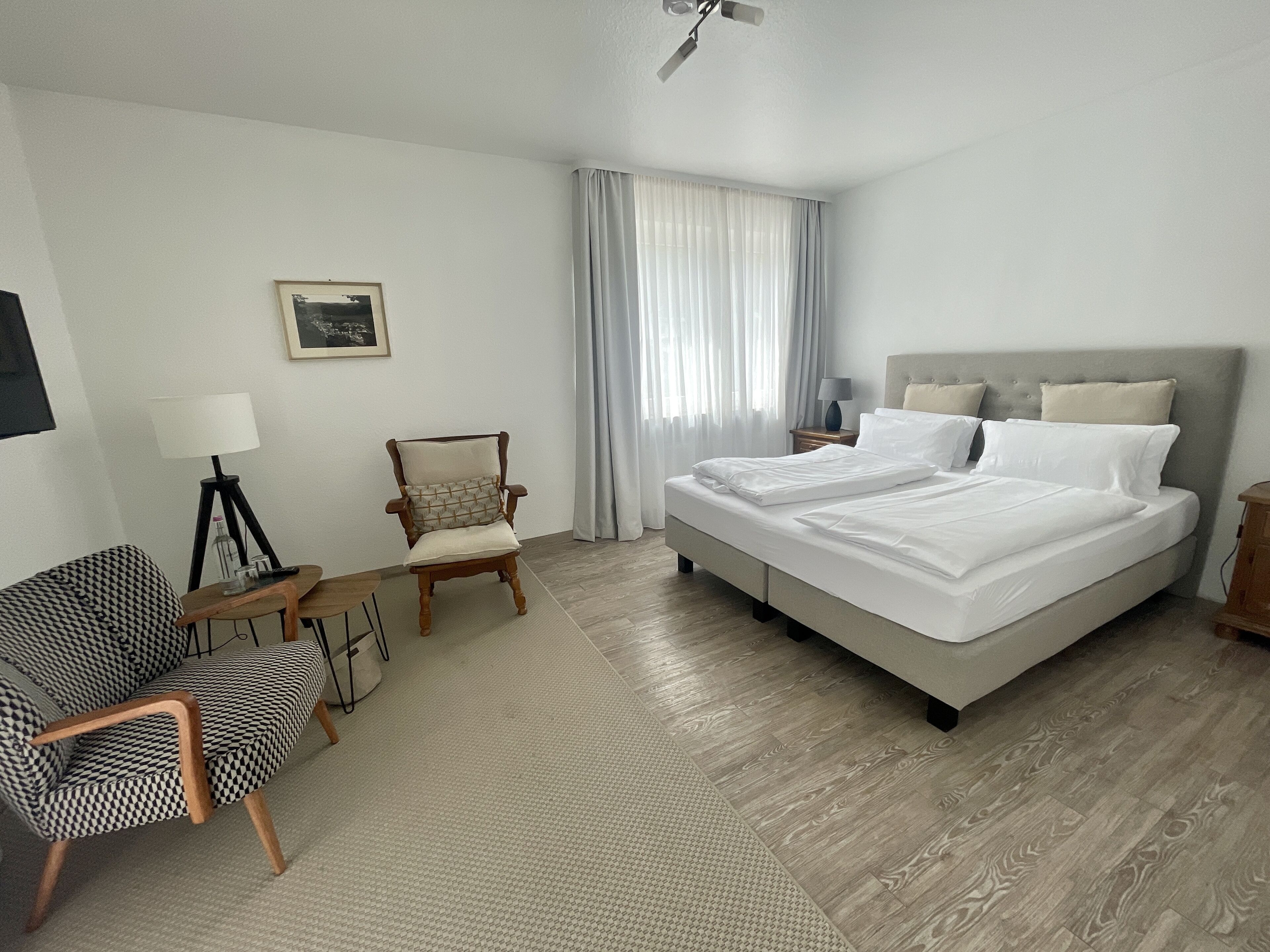 A hotel room with a bed, a chair, a desk, and a lamp.