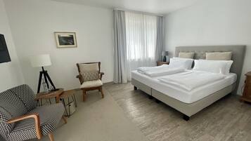 A hotel room with a bed, a chair, a desk, and a lamp.