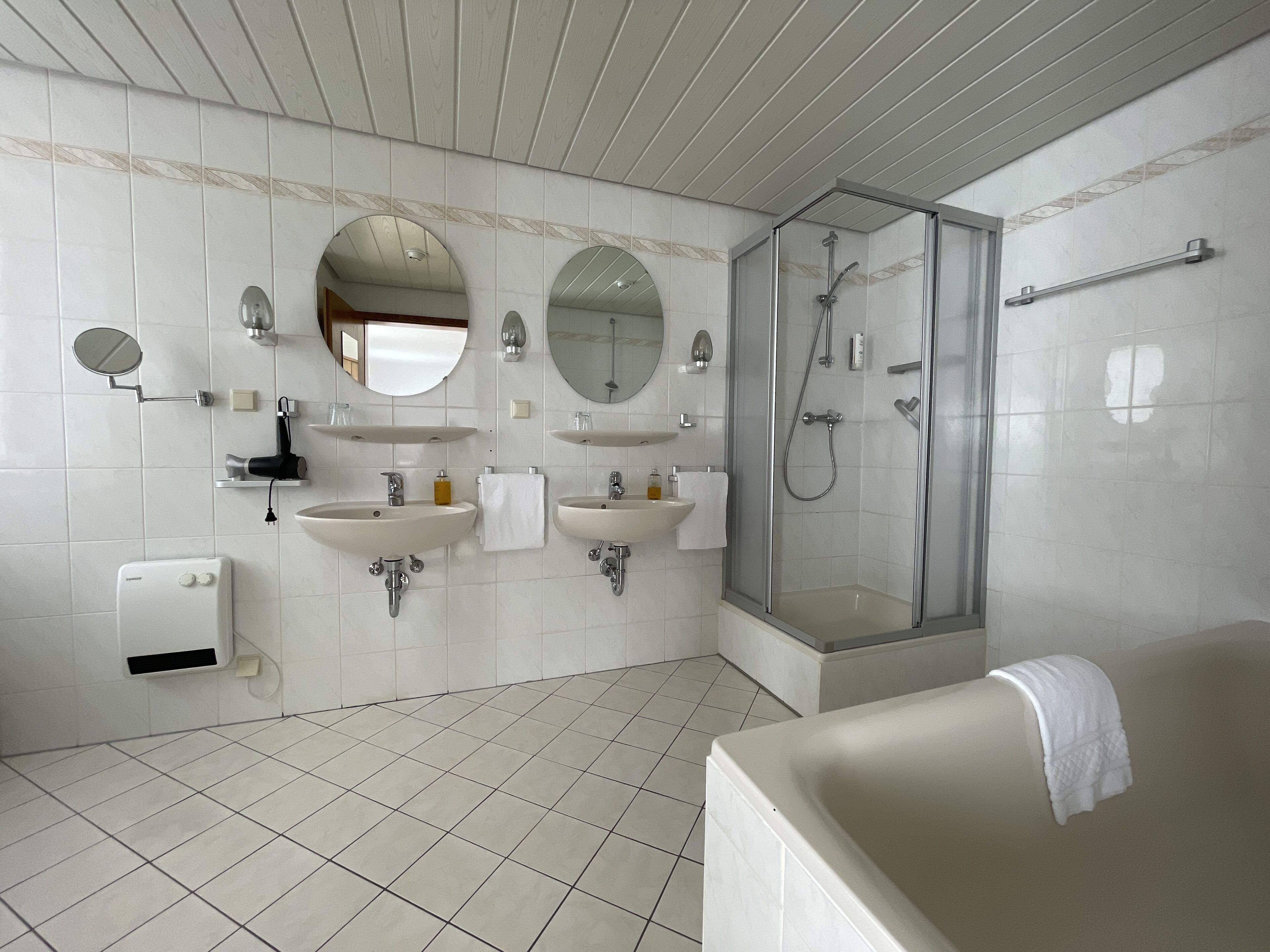 A modern bathroom with two sinks, a glass-enclosed shower, and a bathtub.