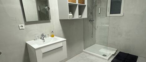 A modern bathroom with a white vanity, a large mirror, a glass-enclosed shower, and black rugs on the floor.