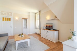 A modern living room with a wooden table, a sofa, a TV on a cabinet, and a door with a window.