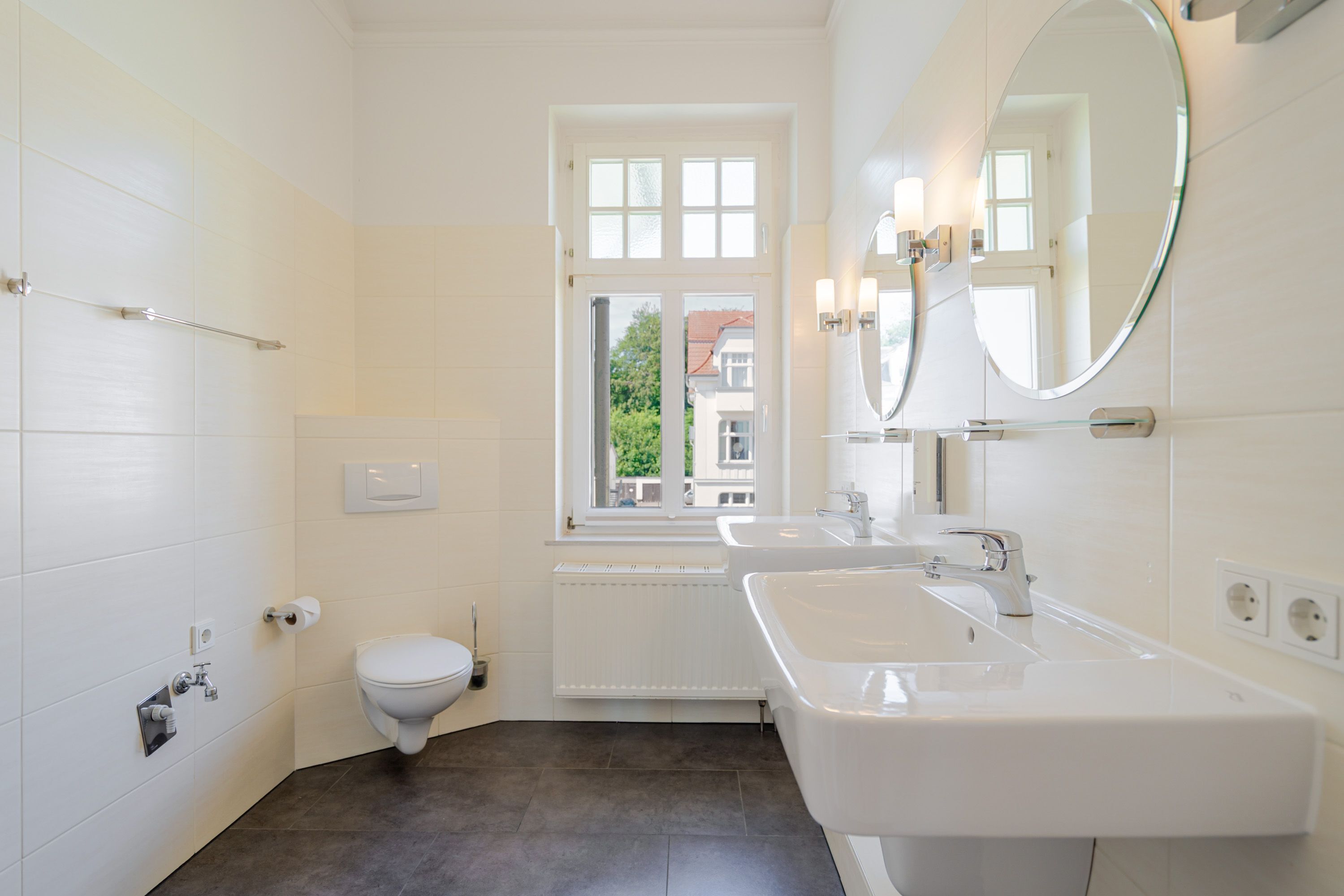 A modern bathroom with a toilet, a window, a sink, and a mirror.