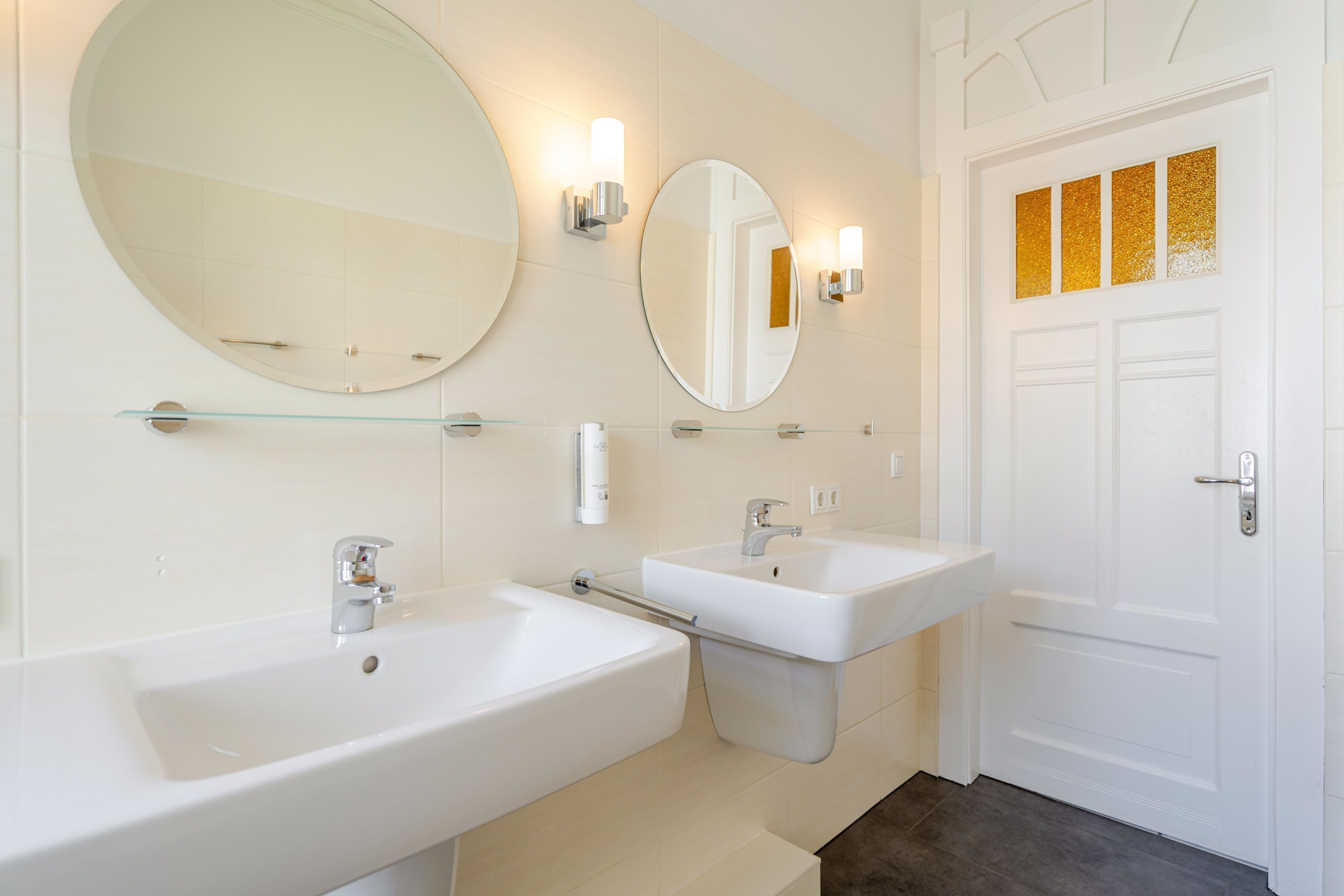 A bathroom with two sinks, a large mirror, and a door with decorative panels.