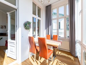 Ein heller Raum mit Esstisch, vier Stühlen, einem Fenster mit Vorhängen und einer Heizung.