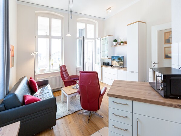 Ein modernes Wohnzimmer mit einer Couch, roten Sesseln, einem Couchtisch und einem Fernseher.
