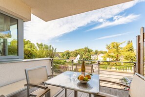 Un balcon avec une table, des chaises, un saladier rempli de fruits et une bouteille.