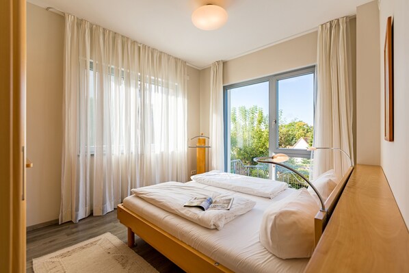 Une chambre avec un grand lit, une fenêtre donnant sur un paysage verdoyant et un petit balcon.