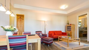 A modern living room with a dining area, a red sofa, striped chairs, and a wooden coffee table. - Quartier II, App. 2.2 (Heringsdorf)