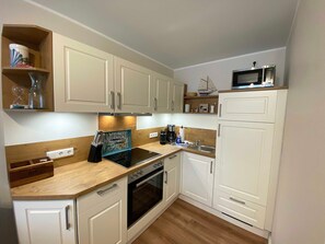 A compact kitchen with white cabinets, a microwave, a sink, and a stove.