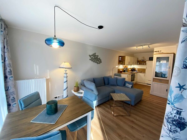 A modern living room with a blue sofa, a wooden dining table, and a kitchen in the background.