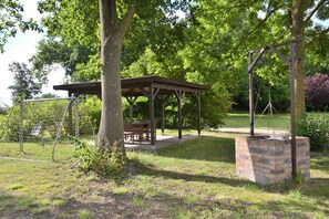 A gazebo with a brick base, surrounded by trees and grass.
