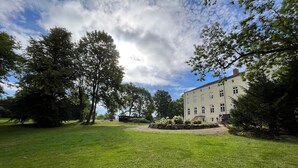 Un grand bâtiment à la façade symétrique, entouré d’une pelouse bien entretenue et d’arbres majestueux.