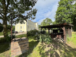 A brick structure with a wooden pergola, a grassy area, and a building in the background. - Apartment Lisa - Castle Gersdorf - T. Schaff (Biendorf)