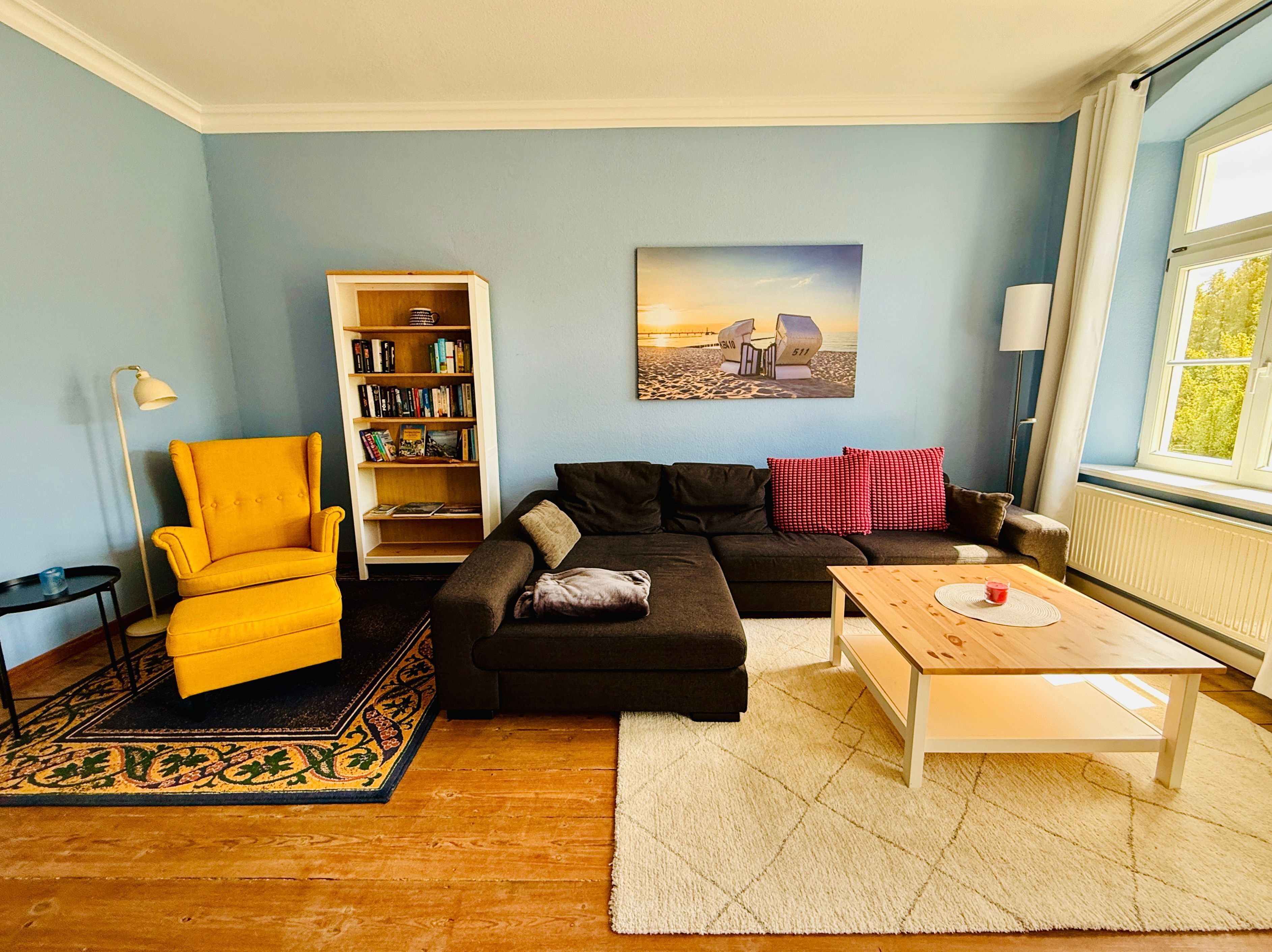 Ein Wohnzimmer mit Sofa, Sessel, Bücherregal und einem Bild an der Wand.