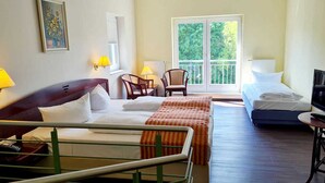 Habitación de hotel con cama, sofá, televisor, sillón y ventana con vistas a zonas verdes.