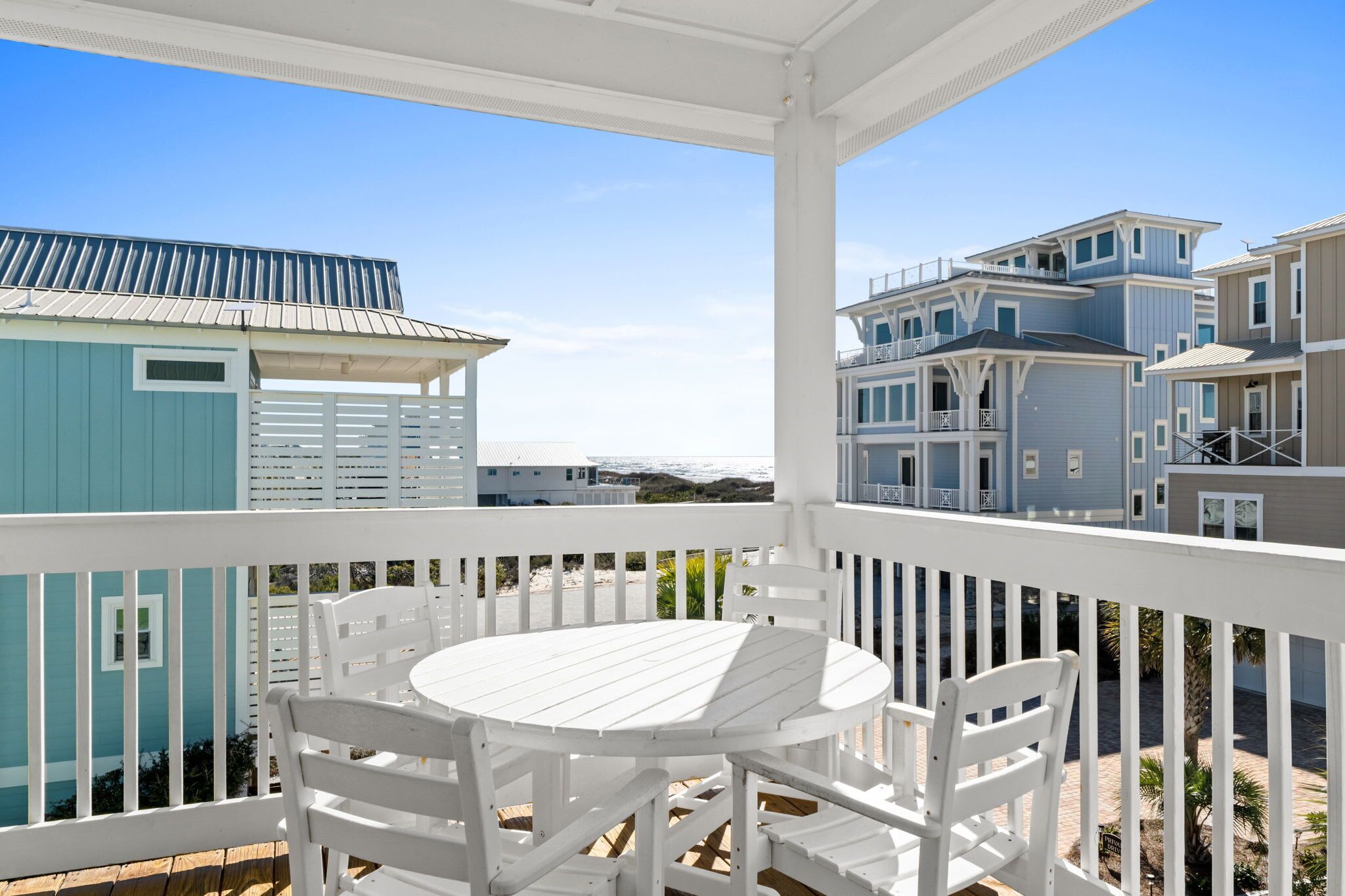 A covered outdoor area with a white table and chairs, overlooking a beachfront property with multiple buildings.