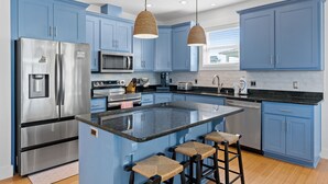 A modern kitchen with blue cabinets, stainless steel appliances, and a central island with bar stools. - Merry Mermaid - Gulf view, Easy beach access, Family and pet friendly (Cape San Blas)