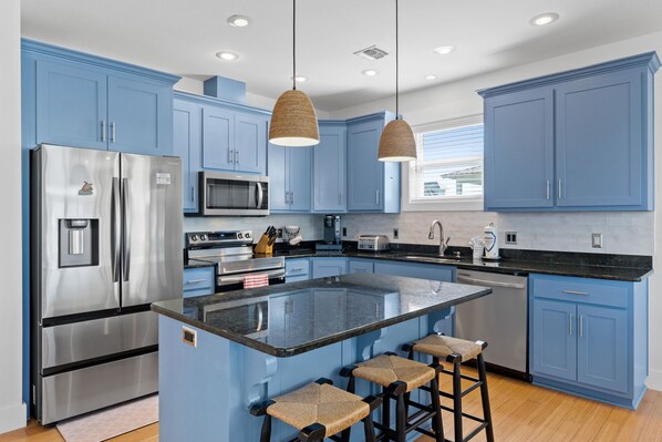 A modern kitchen with blue cabinets, stainless steel appliances, and a central island with bar stools. - Merry Mermaid - Gulf view, Easy beach access, Family and pet friendly (Cape San Blas)