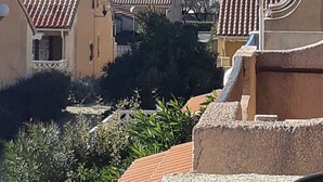 Ein Wohngebiet mit terrakottafarbenen Dächern, einem kleinen Fenster mit blauem Rahmen und einer bergigen Kulisse.