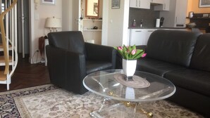 A living room with a black leather sofa, a glass coffee table with a vase of flowers, a patterned rug, and a staircase leading to another room.