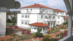 A white building with a red roof, multiple windows, and a small structure with a red roof in front.