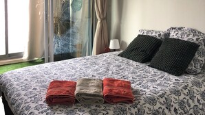 Quarto com cama, luminária no teto, janela com cortinas e um aviso na parede.