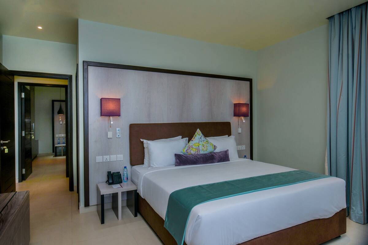 A hotel room with a large bed, two bedside lamps, a nightstand with a phone, and a view of the hallway.