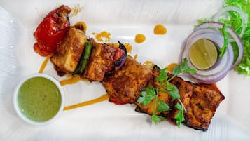 A plate of grilled chicken with vegetables and a side of green sauce.