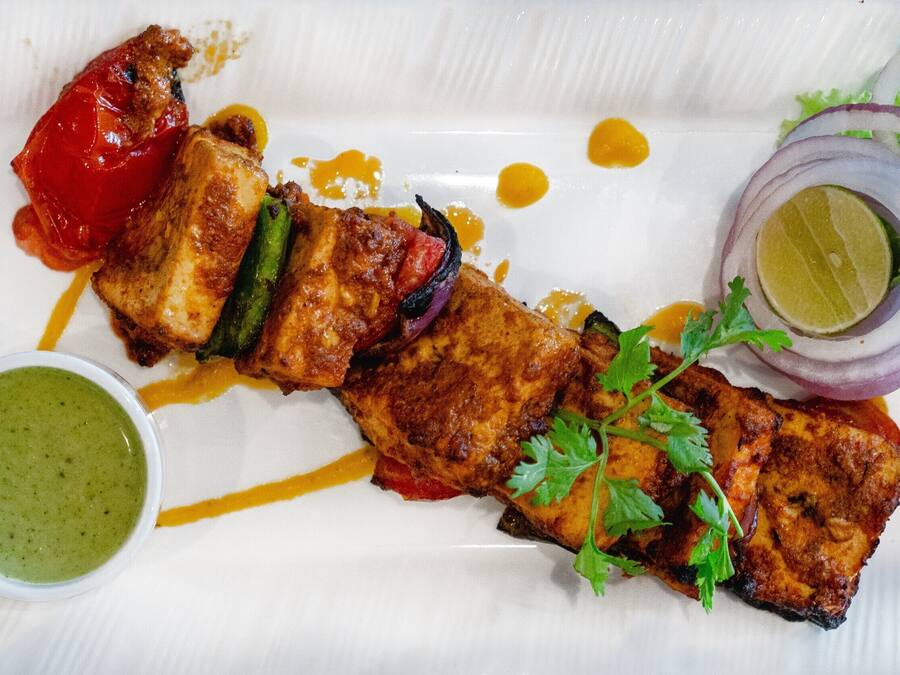 A plate of grilled chicken with vegetables and a side of green sauce.