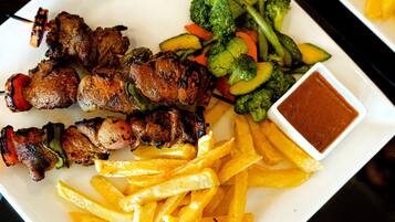 A plate of grilled meat skewers, French fries, and a side of mixed vegetables with a dipping sauce.