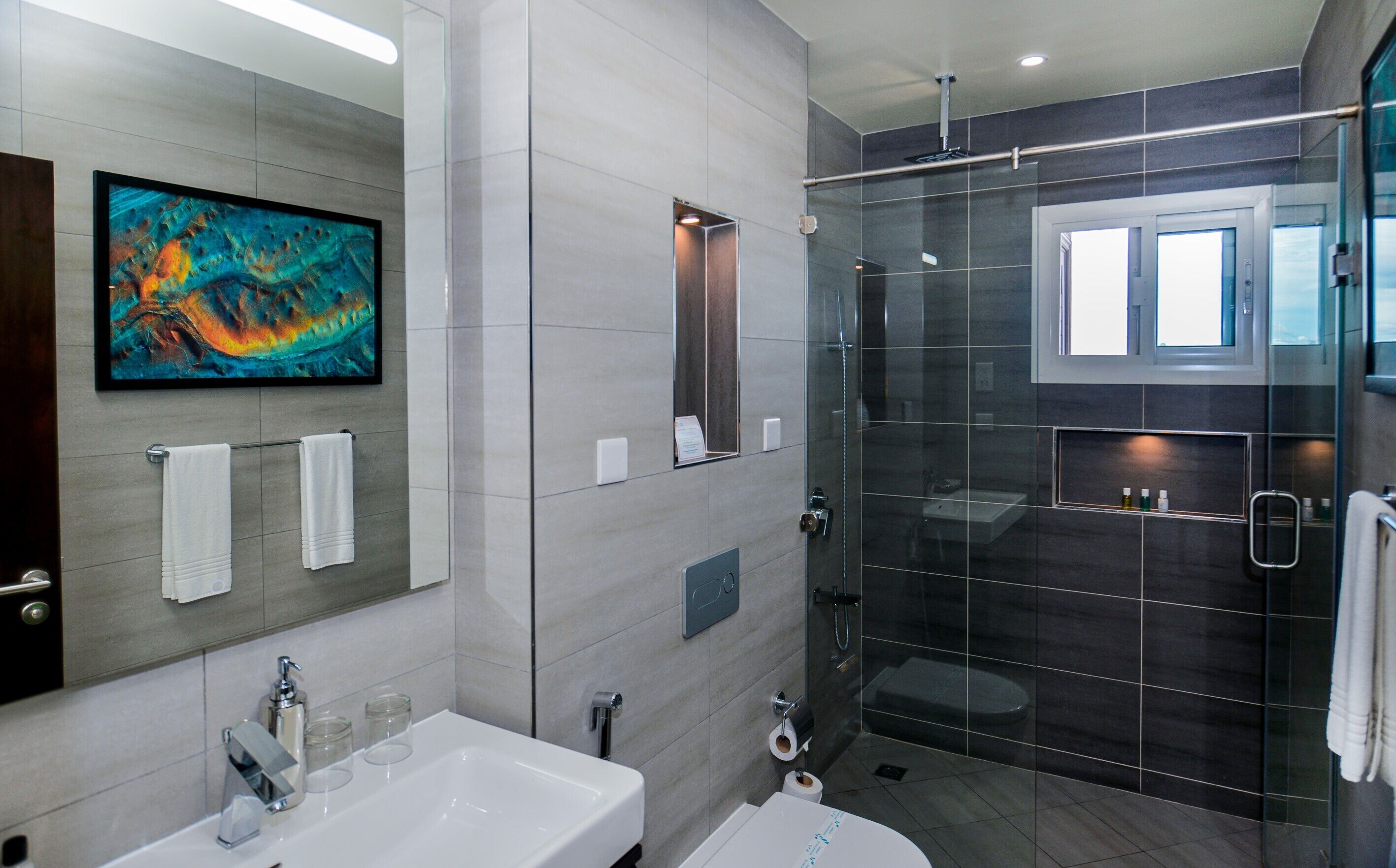 Un baño moderno con ducha de vidrio, un espejo grande y un lavabo con grifo.