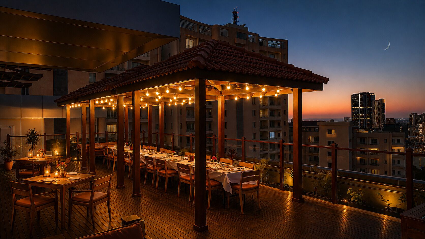 Un espace extérieur aménagé pour les repas, avec des tables et des chaises, une pergola illuminée de guirlandes lumineuses et une vue sur le paysage urbain en arrière-plan.