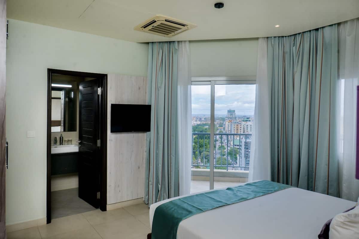 A hotel room with a bed, a bathroom with a mirror, a sink, and a view of a cityscape through a large window.