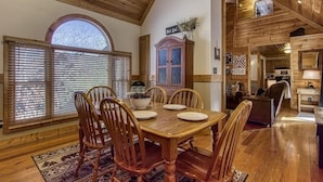 Comedor de madera con una mesa grande y sillas, una ventana con persianas y un armario con un letrero decorativo.