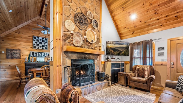 Una sala de estar acogedora con chimenea de piedra, techo de madera y un comedor con un letrero que dice "LET'S EAT".